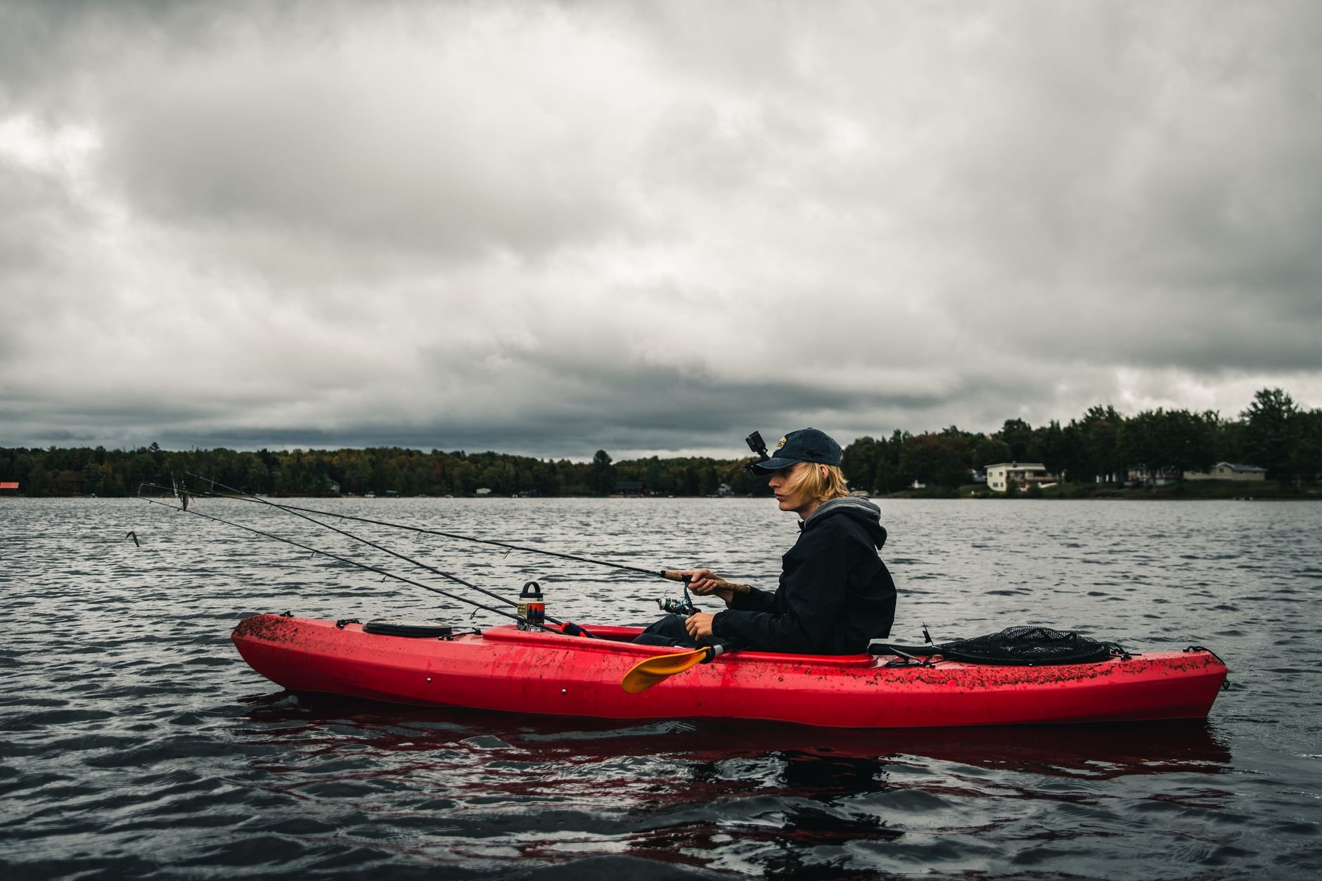 Young man kayak fishing on a serene lake, rod in hand at sunrise